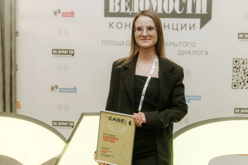 Анна Прохорова с дипломом «Банкротный спор года» на фоне стенда конференции «Ведомостей»